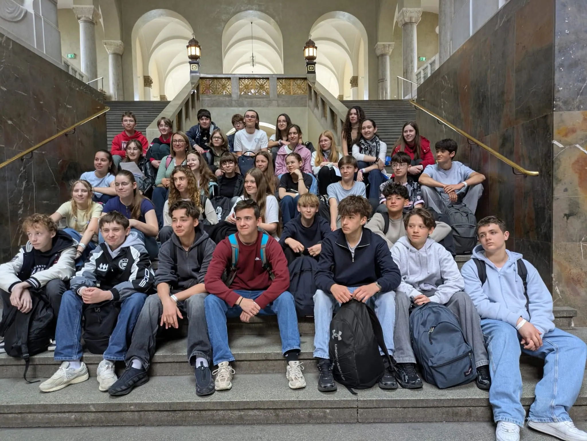 Photo de groupe des élèves du collège Saint-François de Bouvigny-Boyeffles, souriants et assis sur les marches d'un grand escalier en pierre lors de leur visite à Munich.