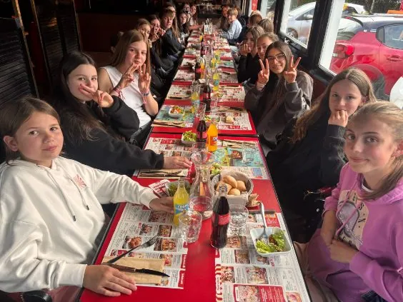 Un groupe d'élèves du collège Saint-François de Bouvigny-Boyeffles sont attablés et prennent un repas ensemble dans une cantine ou un restaurant spacieux, lors de leur voyage scolaire en Loire Atlantique. Plusieurs sourient face à l'objectif.