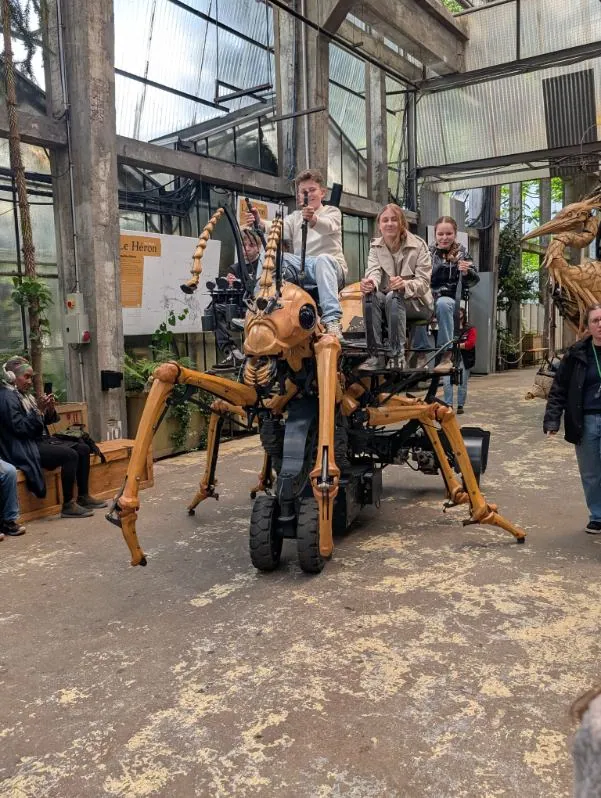 Quatre élèves du collège Saint-François de Bouvigny-Boyeffles sont installés sur le dos d'une gigantesque fourmi mécanique, une structure articulée en bois et métal, à l'intérieur d'un atelier-serre à Nantes (Les Machines de l'Ile).