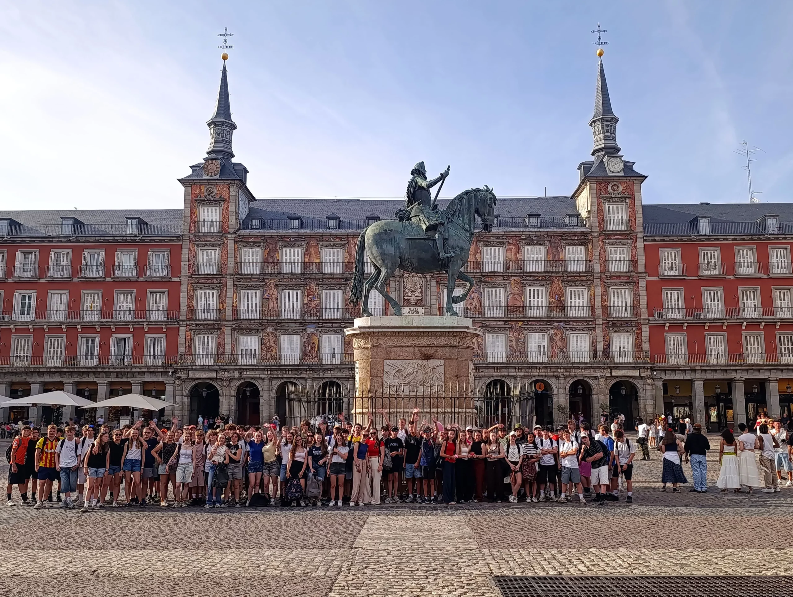 Groupe d'élèves du collège posant devant la statue équestre sur la Plaza Mayor lors d'un voyage scolaire à Madrid.
